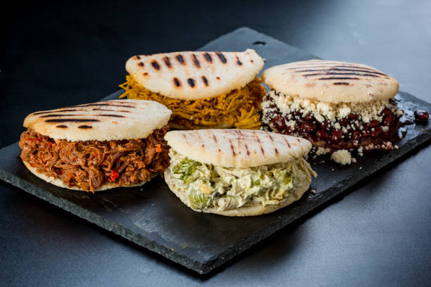 Venezuelan Latin American food, 4 arepas of different stuffing on a black table. Arepa with mechada meat, queen pepeada, black beans with white cheese and chicken stock photo