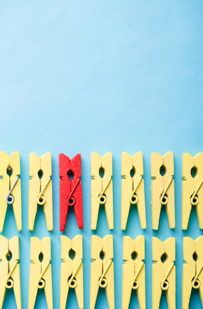 Stand out from the crowd and different concept. Leadership and other similar concepts. One red clothespin stands out from other yellow clothespins on blue background.