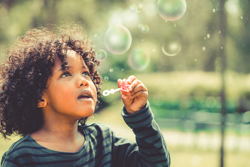 Happy little kid blowing soap bubble in school garden. Child outdoor activity concept.