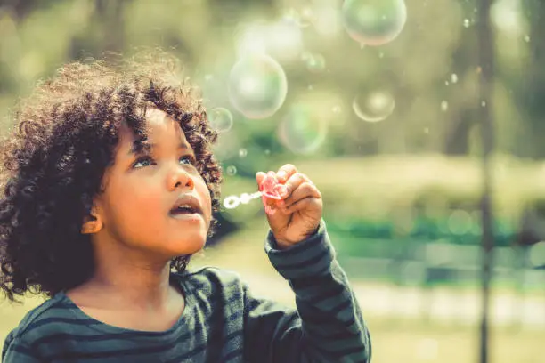 Photo of Happy little kid blowing bubble in school garden.