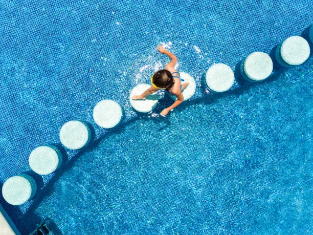 Little girl crossing swimming pool on stepping stones