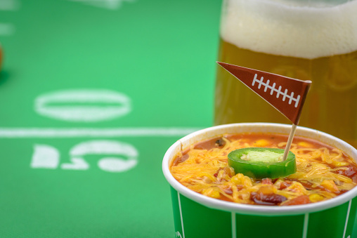 macro closeup of small bowl of chili and beer mug on table decorated for big football game