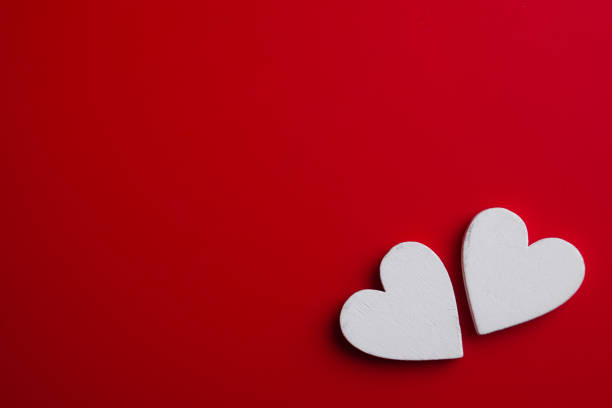 Two white wooden hearts on red background. Top view Valentines pattern. stock photo