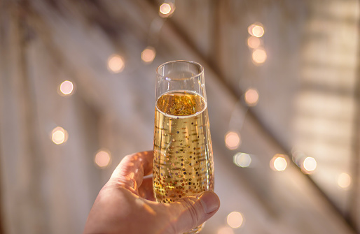 hand rasing a glass of champagne for a toast with twinkling lights in background