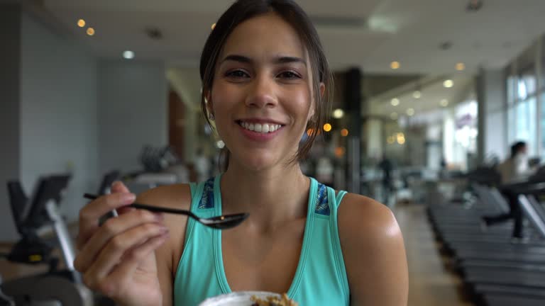 Beautiful fit woman at the gym taking a break eating a parfait while facing camera smiling