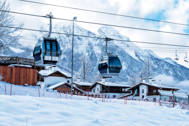 cabinovia, villaggio e alta catena montuosa in una limpida giornata di sole in inverno - european alps cold mountain range clear sky foto e immagini stock