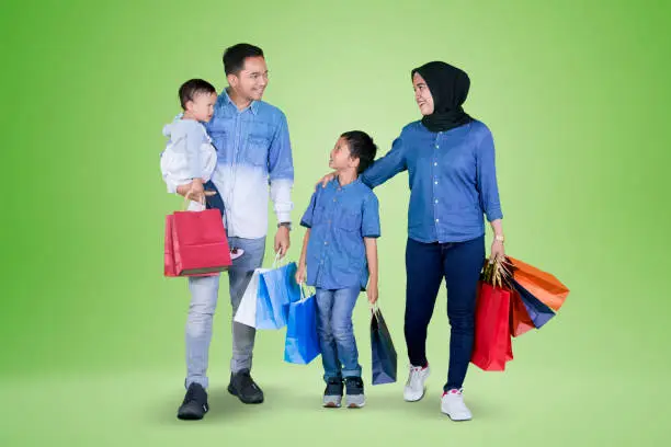 Picture of young happy family carrying shopping bags while walking together in the studio with green screen