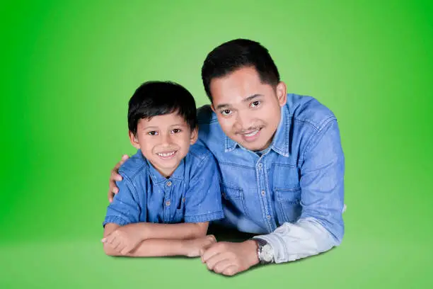 Picture of happy father embracing his son while lying together in the studio with green screen