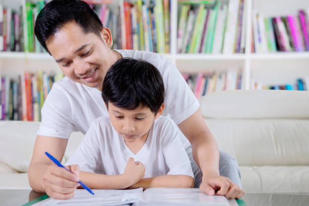 istock Little boy guided by his father to read a book 1124340770