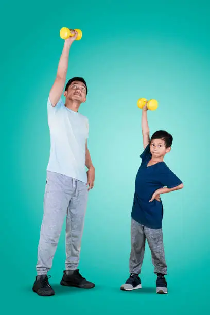 Full length of an Asian man with his son lifting a dumbbell while exercising together in the studio