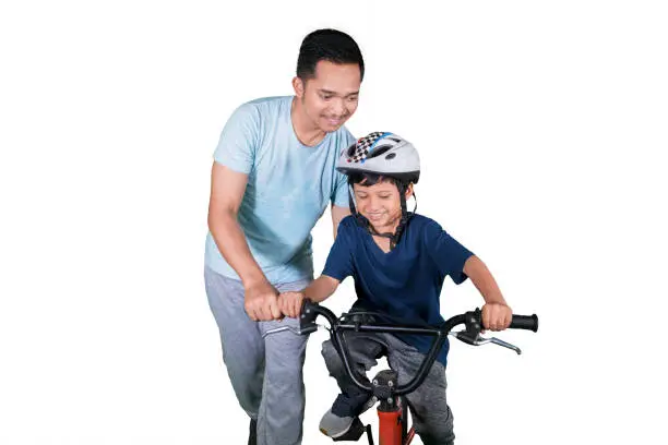 Picture of happy little boy learning to ride a bike with his father in the studio, isolated on white background
