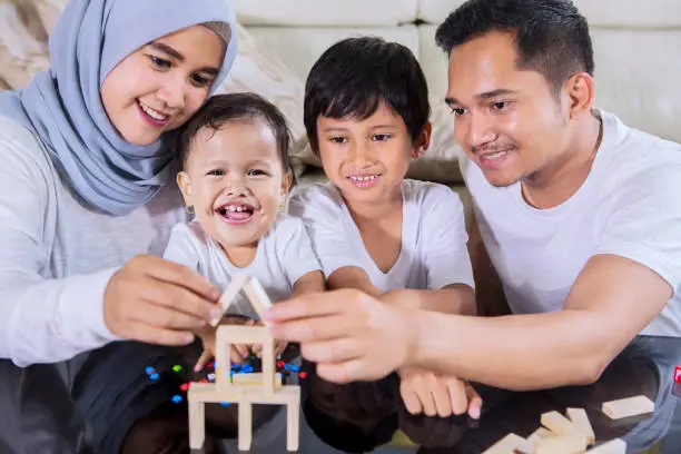Image of happy family playing with wood blocks to build a dream house while sitting in the living room