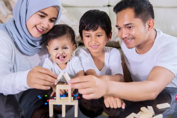 Image of happy family playing with wood blocks to build a dream house while sitting in the living room