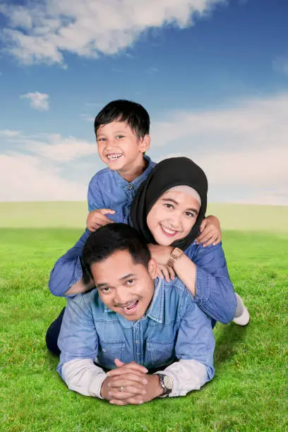 Portrait of Muslim family smiling at the camera while lying together in the meadow