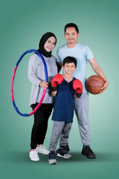 Full length of happy family holding different sports equipment while standing together in the studio