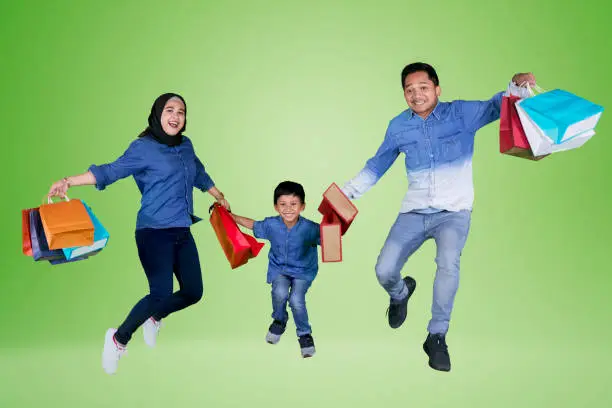 Picture of happy family holding shopping bags while jumping together in the studio, shot with green screen