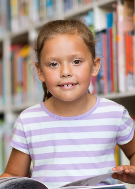 istock Cute girl reading book in school library 1124354590