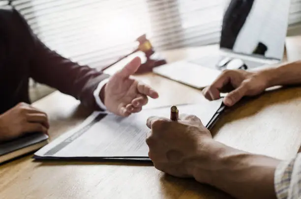 Photo of client customer signing contract and discussing business with legal consultants, notary or justice lawyer with laptop computer and wooden judge gavel on desk in courtroom office, legal service concept