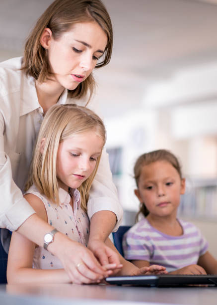 istock Teacher assisting girl in typing at computer lab 1124354695