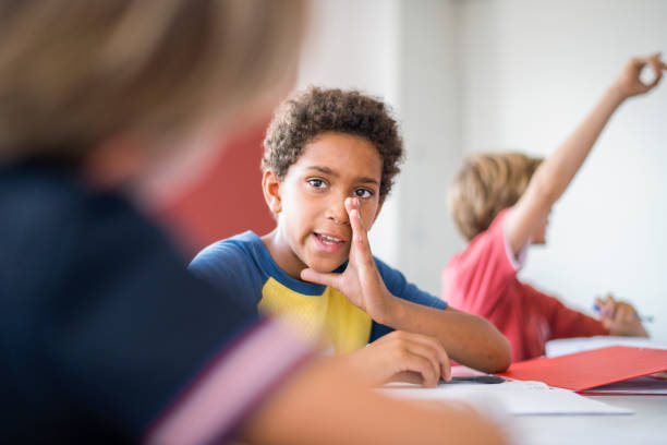 istock Elementary boy whispering to friend in classroom 1124355761
