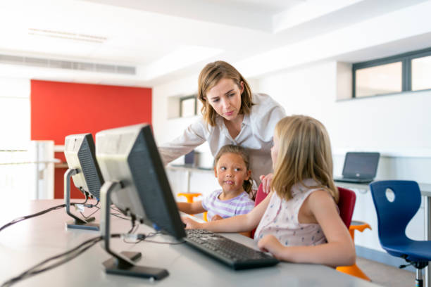 profesor ayudando a niñas primaria en el laboratorio de computación - computer lab child internet development fotografías e imágenes de stock