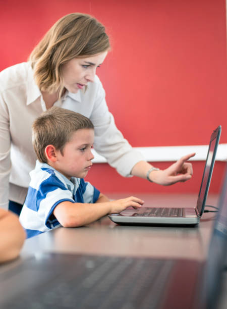 nauczyciel pomaga chłopcu za pomocą laptopa przy biurku - computer lab child internet development zdjęcia i obrazy z banku zdjęć