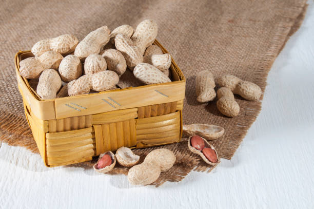 istock Groundnuts in bowl and on burlap, white wooden table. 1124357577