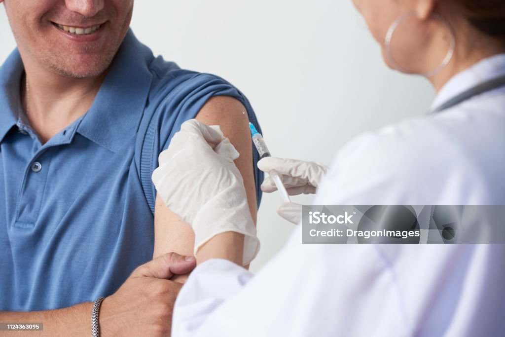 Vaccinating patient Doctor vaccinating smiling man patient in clinic Vaccination Stock Photo