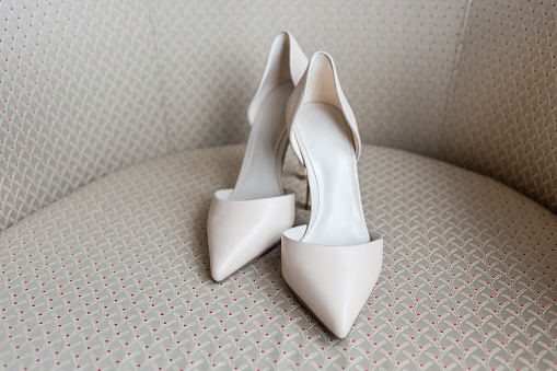 Pair of white shoes commonly called D'Orsay on beige chair.