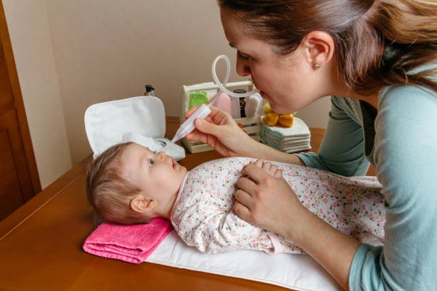 mother using the nasal aspirator with her baby - shoe women adult baby imagens e fotografias de stock