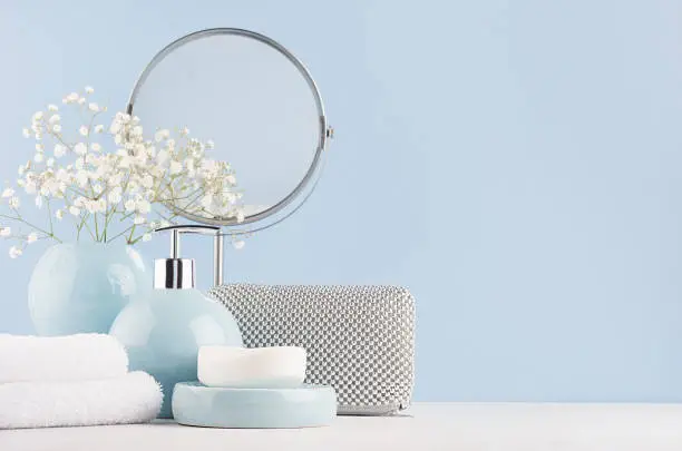 Photo of Dressing table with circle mirror, cosmetic silver accessories and white small flowers in ceramic pastel blue vase on white wood board.