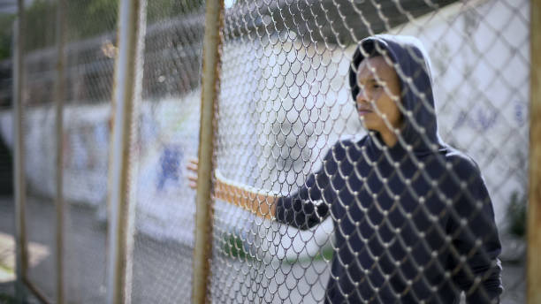 拘束、フェンスの背後にあるアフリカ系アメリカ人の少年の家族から区切られた移民の子 - 孤児 ストックフォトと画像