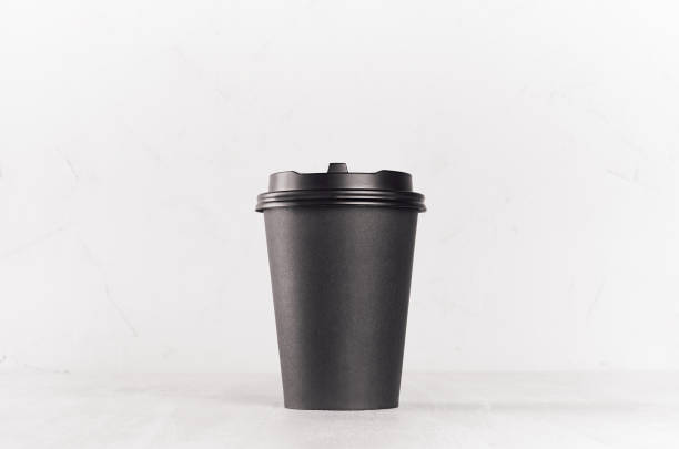 istock Coffee mockup -  big blank black paper cup with cap on white wood table, coffee shop interior. Modern elegant concept for branding identity, advertising, design. 1124376598