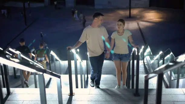 Carefree couple walking upstairs to watch illuminated night city, romantic date