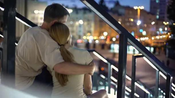 Couple sitting and hugging on stairs, enjoying beautiful city view, romantic