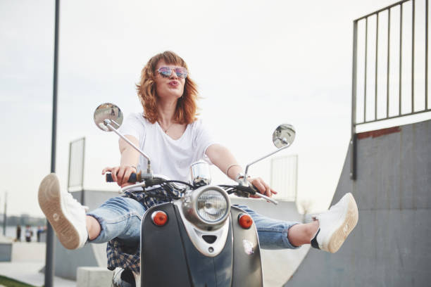 Portrait of a beautiful girl hipster sitting on a black retro scooter, smiling posing and enjoy the warm spring sunshine. Portrait of a beautiful girl hipster sitting on a black retro scooter, smiling posing and enjoy the warm spring sunshine moped stock pictures, royalty-free photos & images