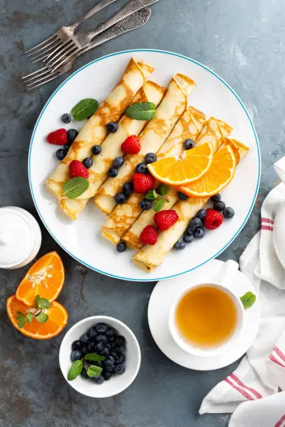 Sweet pancakes wrapped with fresh berries, crepes with blueberry and raspberry on breakfast, top view