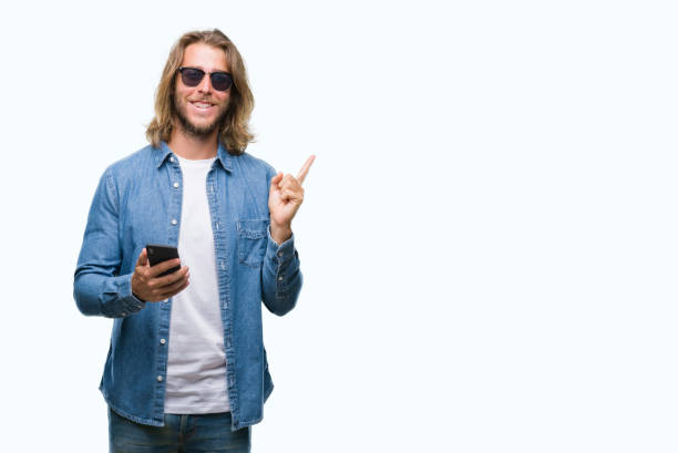 istock Young handsome man with long hair over isolated background sending message using smartphone very happy pointing with hand and finger to the side 1124388949