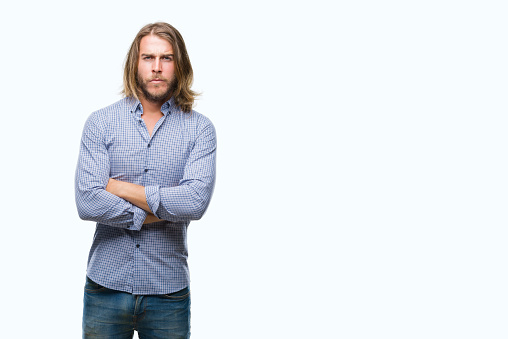 Young handsome man with long hair over isolated background skeptic and nervous, disapproving expression on face with crossed arms. Negative person.