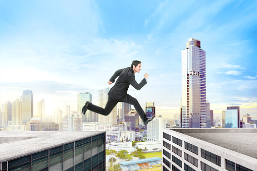 Handsome asian businessman jumping over building gap on the city