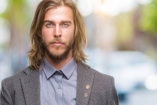 istock Young handsome business man with long hair over isolated background with serious expression on face. Simple and natural looking at the camera. 1124390620