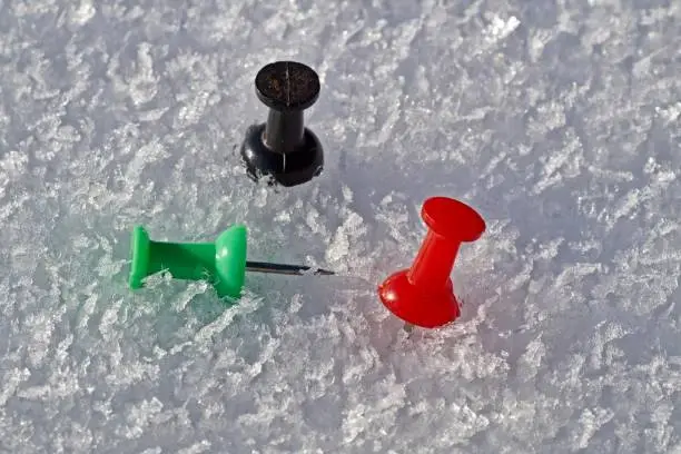 Thumbtack in the colors red, black and green isolated on a snow background