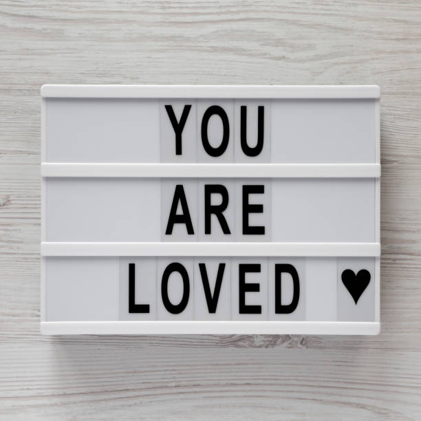 istock Modern board with text 'You are loved' on a white wooden background, top view. Flat lay, overhead. Close-up. 1124391354