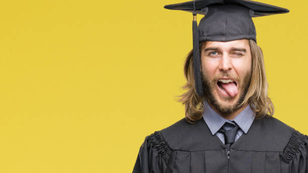 Young handsome graduated man with long hair over isolated background sticking tongue out happy with funny expression. Emotion concept. Young handsome graduated man with long hair over isolated background sticking tongue out happy with funny expression. Emotion concept. protruding stock pictures, royalty-free photos & images