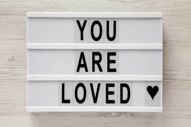 istock Modern board with text 'You are loved' on a white wooden surface, top view. Flat lay, overhead. Closeup. 1124391758