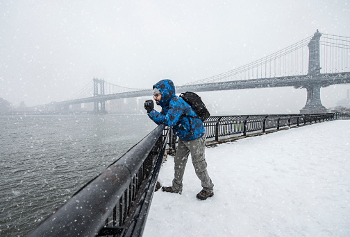 Travel photographer working in New York in a heavy snow in winter, Manhattan Bridge seen on the background