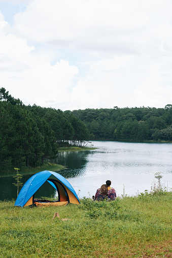 Young couple camping by lake, view from the back