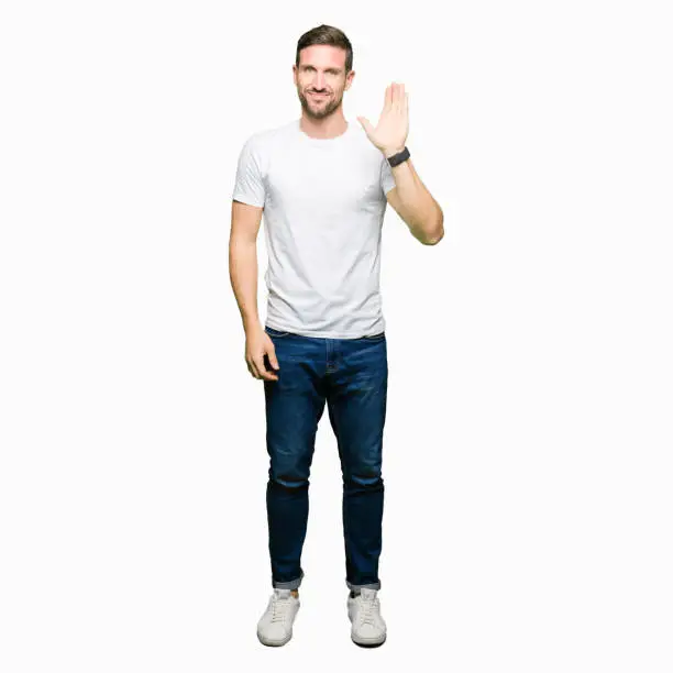 Photo of Handsome man wearing casual white t-shirt Waiving saying hello happy and smiling, friendly welcome gesture