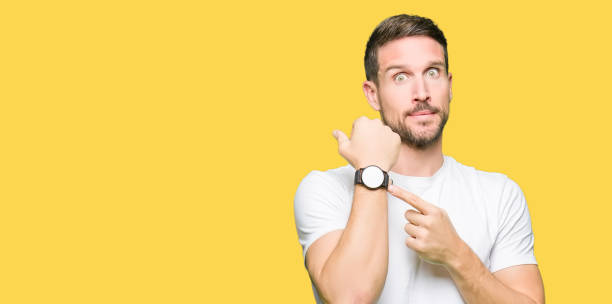 handsome man wearing casual white t-shirt in hurry pointing to watch time, impatience, upset and angry for deadline delay - clock face fotos imagens e fotografias de stock