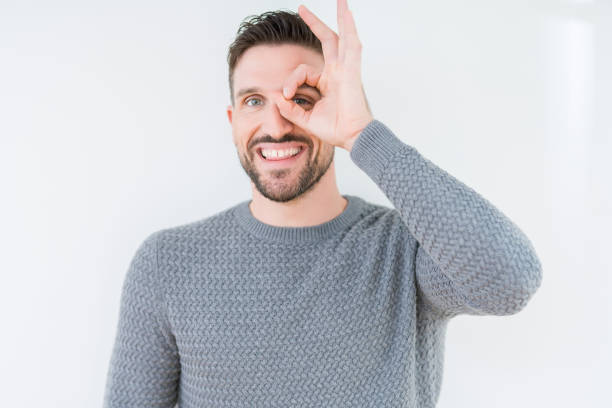istock Young handsome man wearing casual sweater over isolated background doing ok gesture with hand smiling, eye looking through fingers with happy face. 1124394018